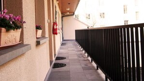 A covered corridor with a wooden ceiling, potted plants, a fire extinguisher, and a black railing. - Hotel Beaulieu (Clermont-Ferrand)