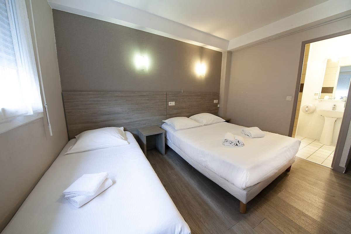 A hotel room with two single beds, a nightstand, a wall-mounted light, and a bathroom visible through an open door.
