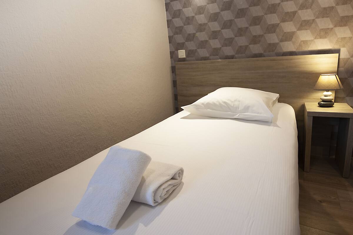 A neatly made bed with a white towel, a wooden headboard, and a bedside table with a lamp.