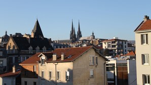 A cityscape with a prominent church spire and residential buildings with red-tiled roofs. - Hotel Beaulieu (Clermont-Ferrand)