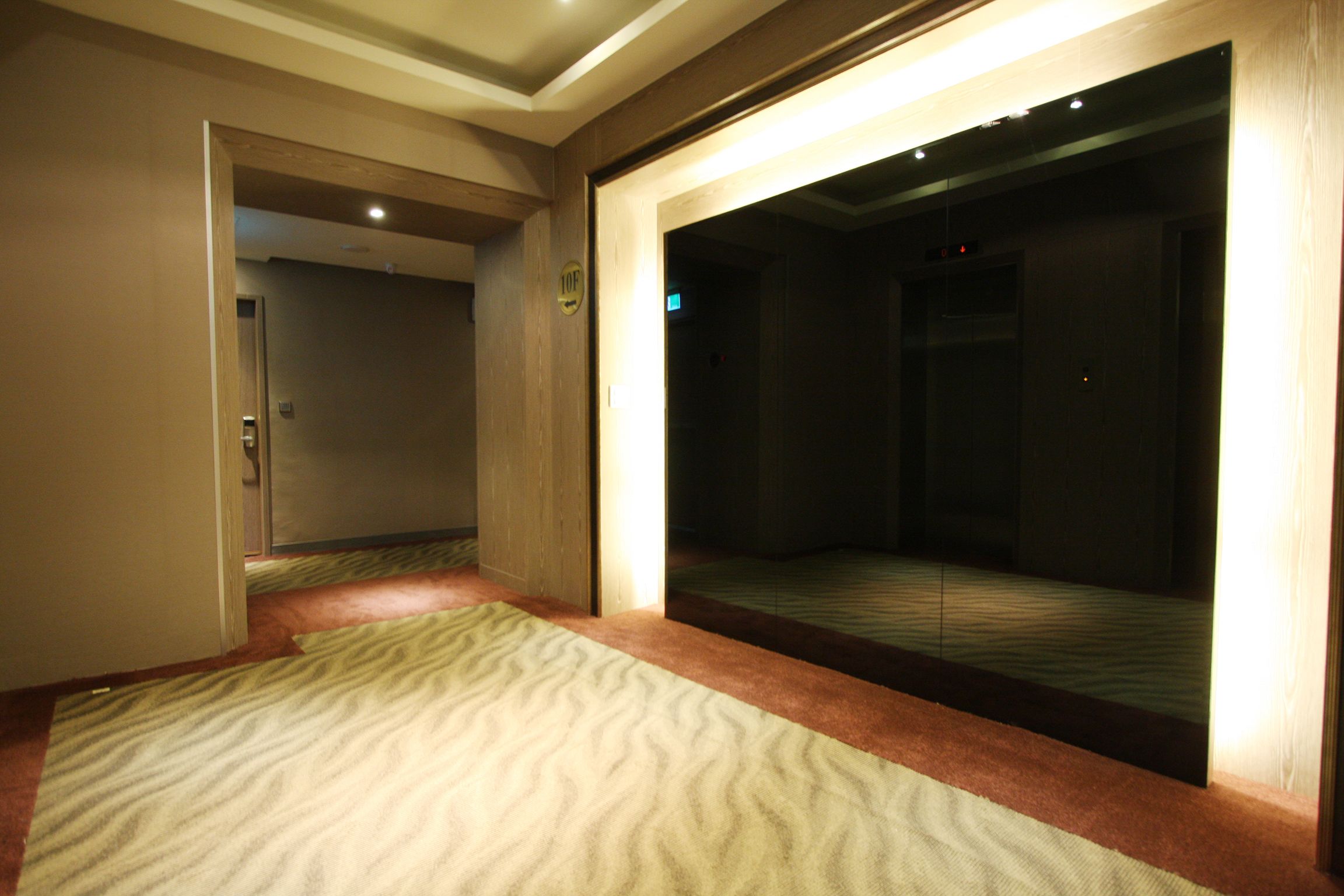 A hotel room with a carpeted floor, a wooden door, and a mirror reflecting the room.