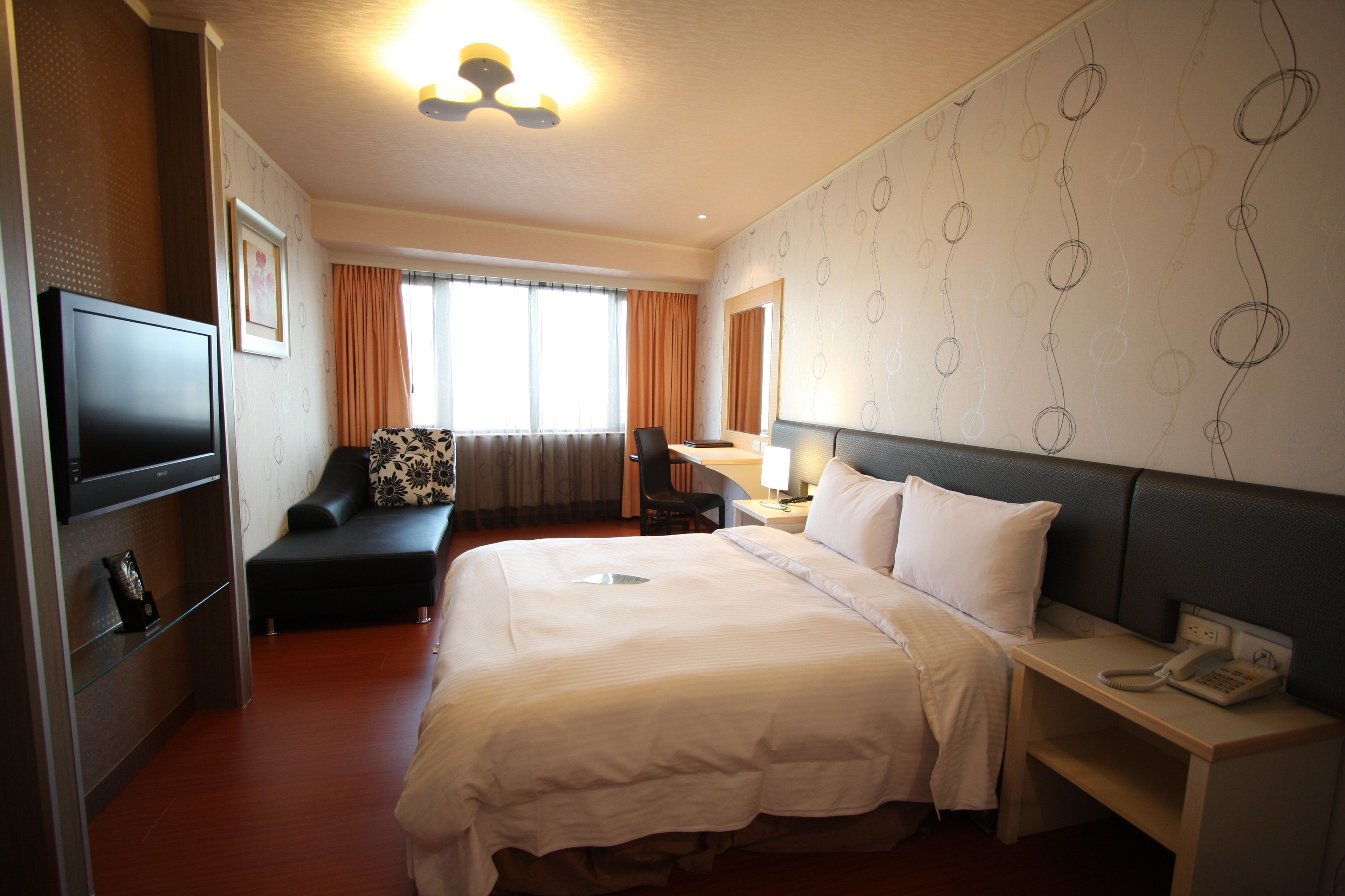 A hotel room with a bed, a desk, a chair, a TV, and a phone.