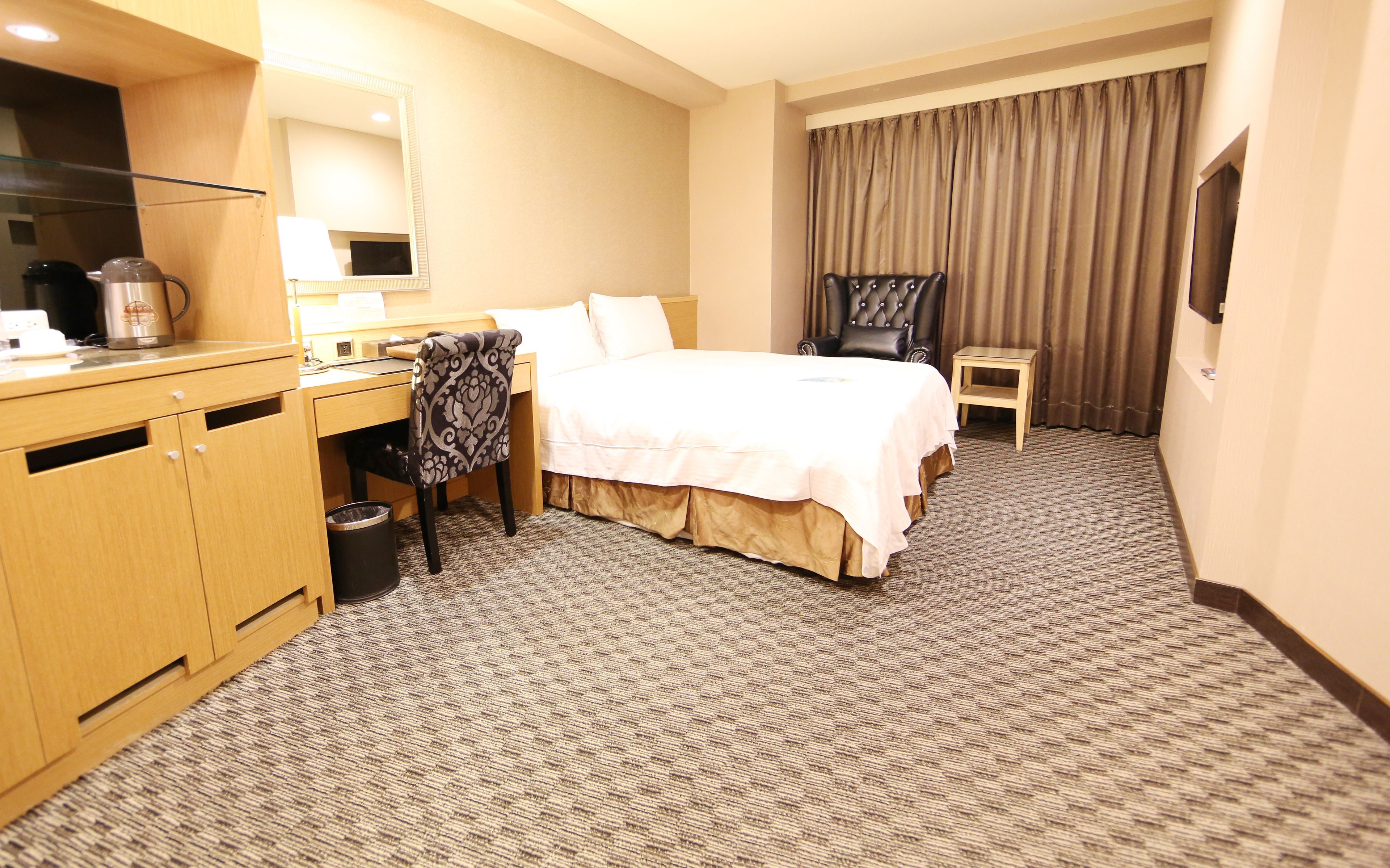 A hotel room with a bed, a desk, a chair, a TV, and a trash can.