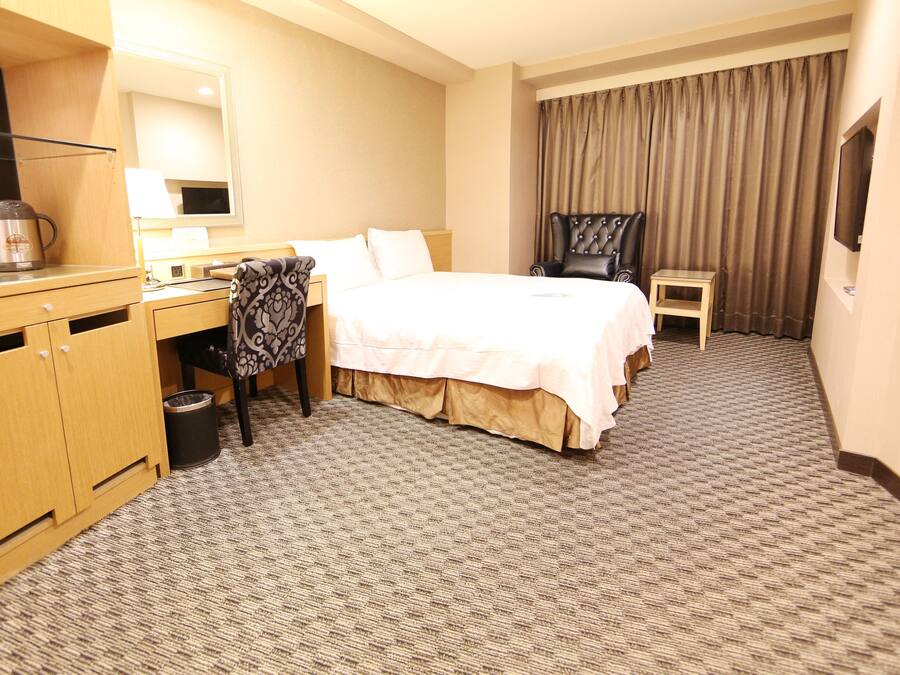 A hotel room with a bed, a desk, a chair, a TV, and a trash can.