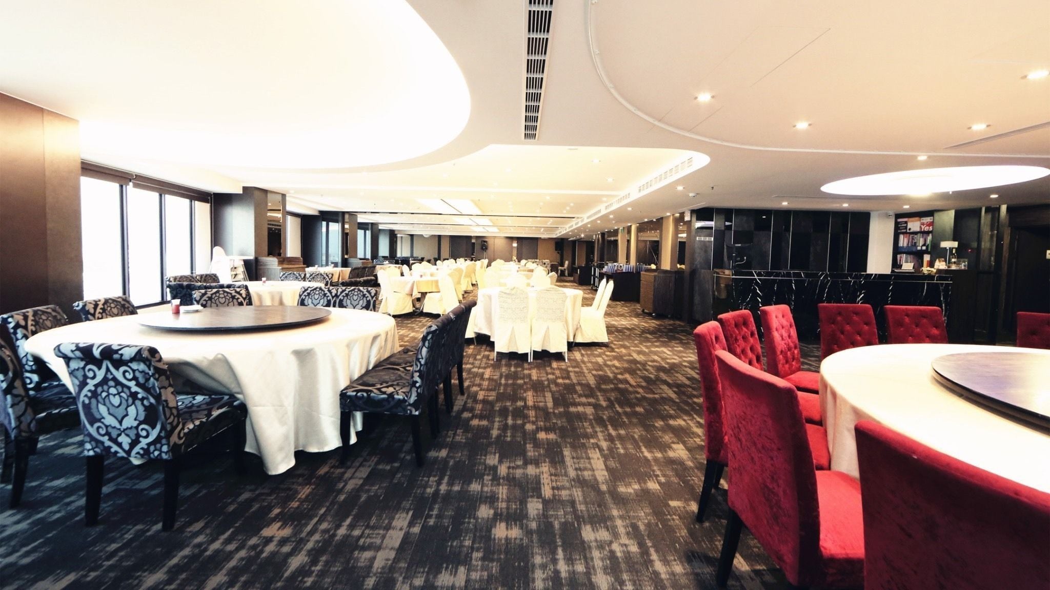 A hotel conference room with round tables, chairs, and a bar area.
