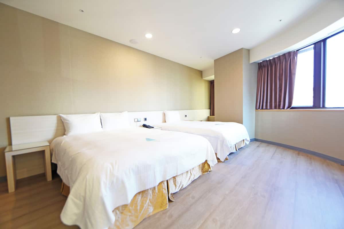 Een hotelkamer met twee bedden, een klein nachtkastje en een groot raam met gordijnen.