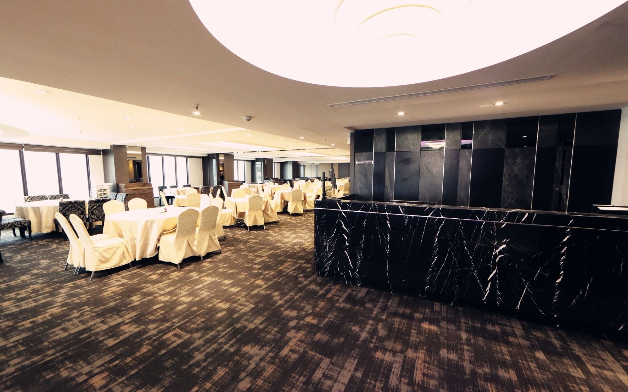 Uma sala de conferência com mesas e cadeiras redondas, um balcão de mármore e uma janela grande.