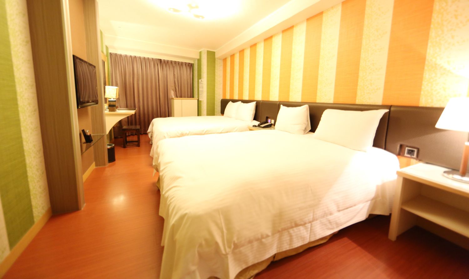 Habitación de hotel con dos camas, televisor, escritorio y lámpara.