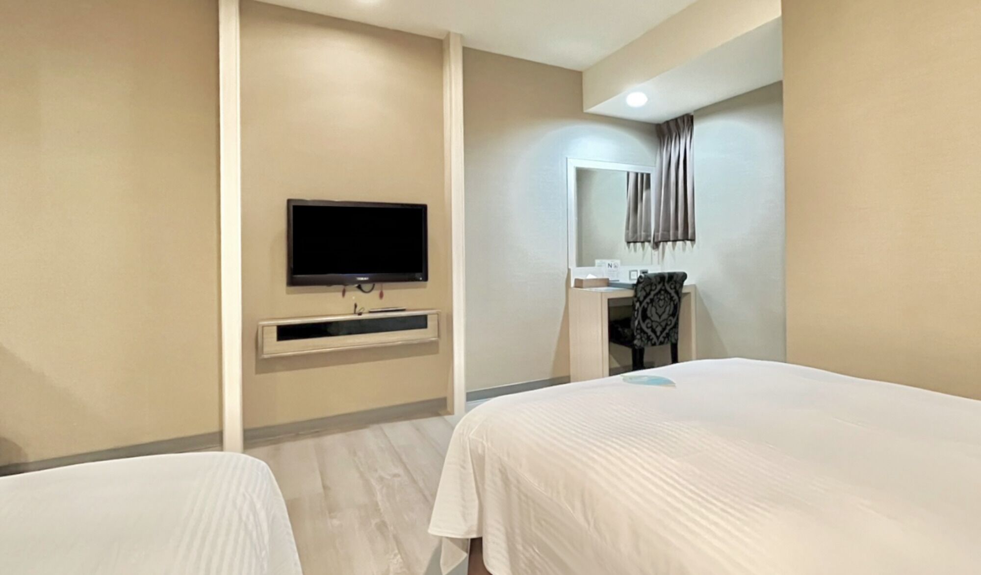 A hotel room with two beds, a TV mounted on the wall, and a small desk with a chair.