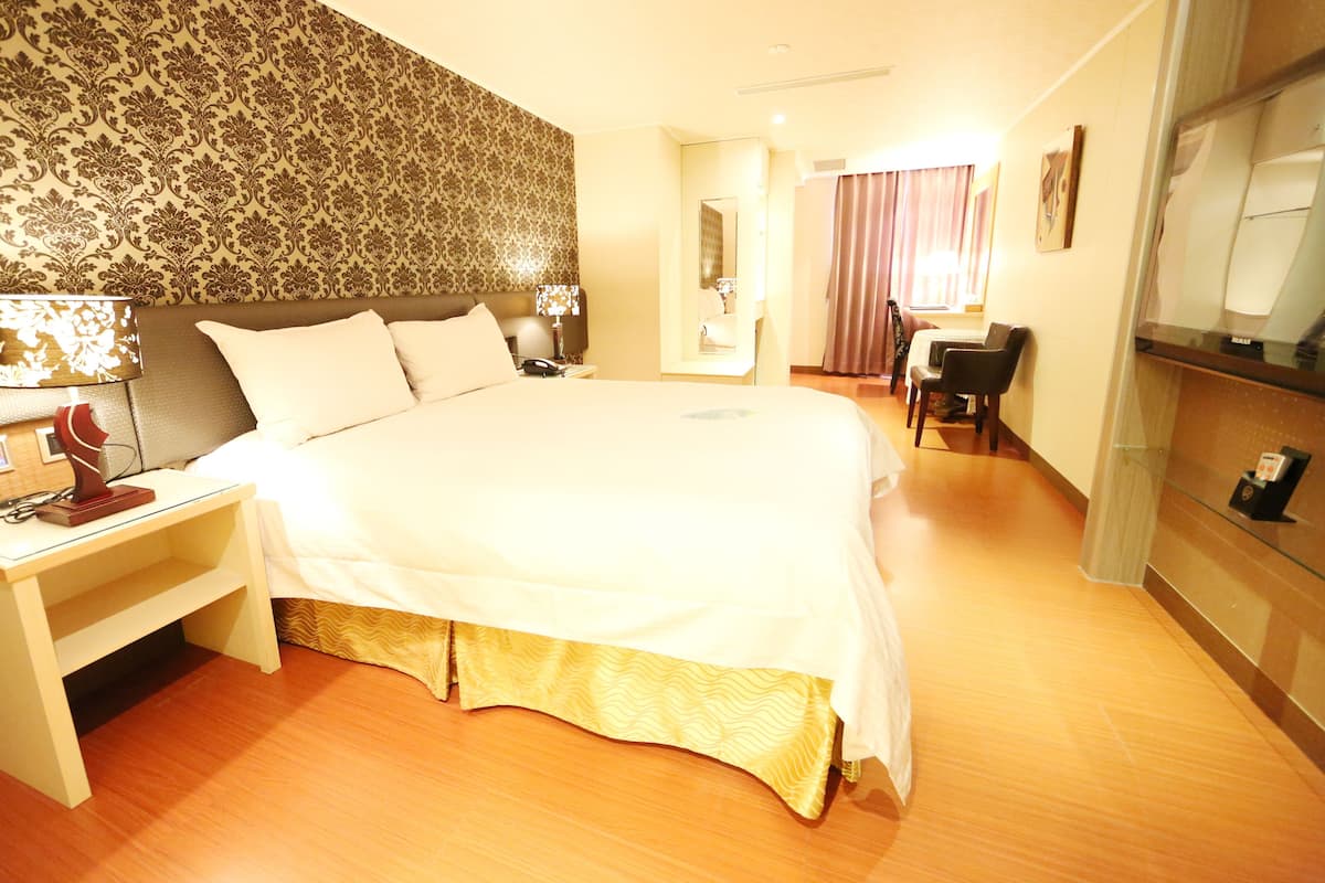 Een hotelkamer met een groot bed, een bureau met lamp, een stoel en een spiegel.