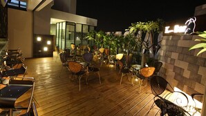 An outdoor patio area with wooden flooring, metal chairs, and tables. There are potted plants and a neon sign in the background. - Grand Earl Hotel (Douliou)