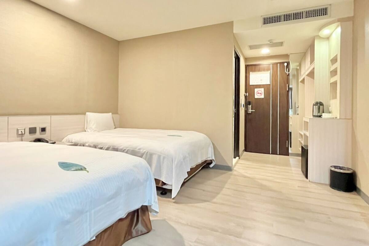 Een hotelkamer met twee bedden, een houten vloer, een deur met een rookvrij sign en een kleine prullenbak.
