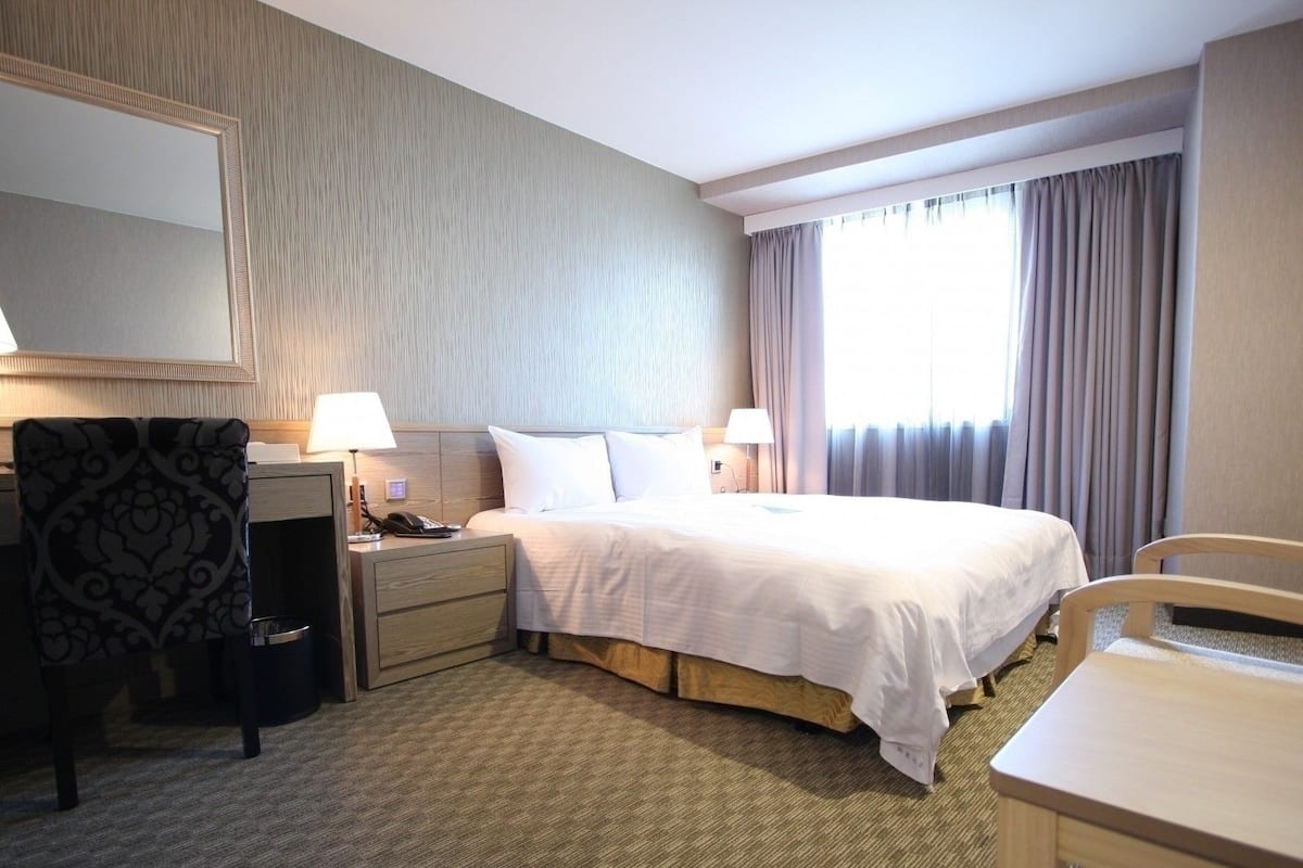Een hotelkamer met een bed, nachtkastjes, een bureau, een stoel, een spiegel en een raam met gordijnen.