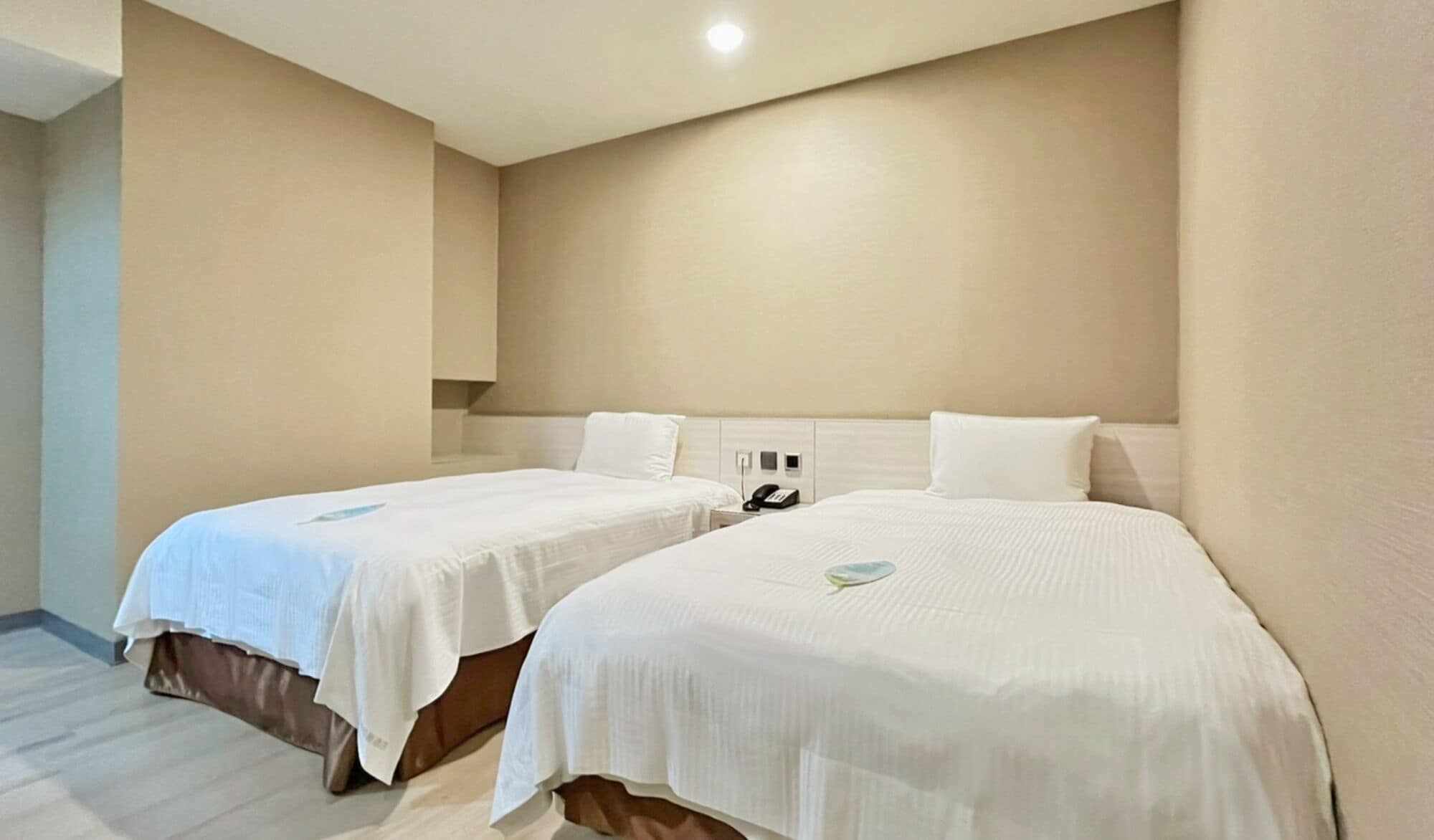 A hotel room with two beds, a bedside telephone, and a light switch on the wall.