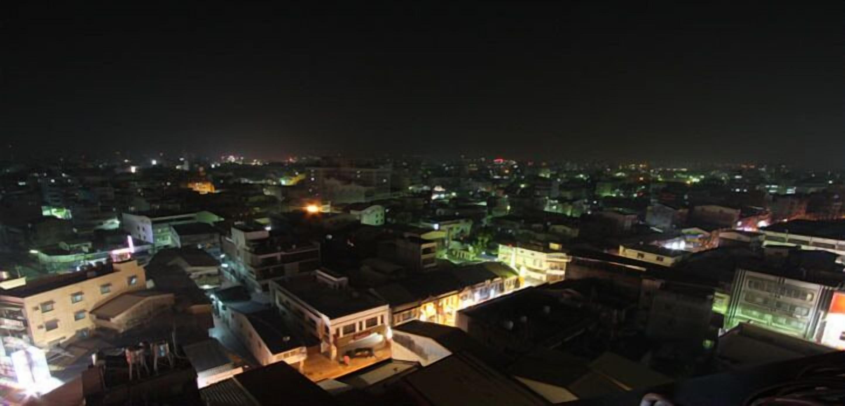 A nighttime cityscape with illuminated buildings and a dense urban layout.