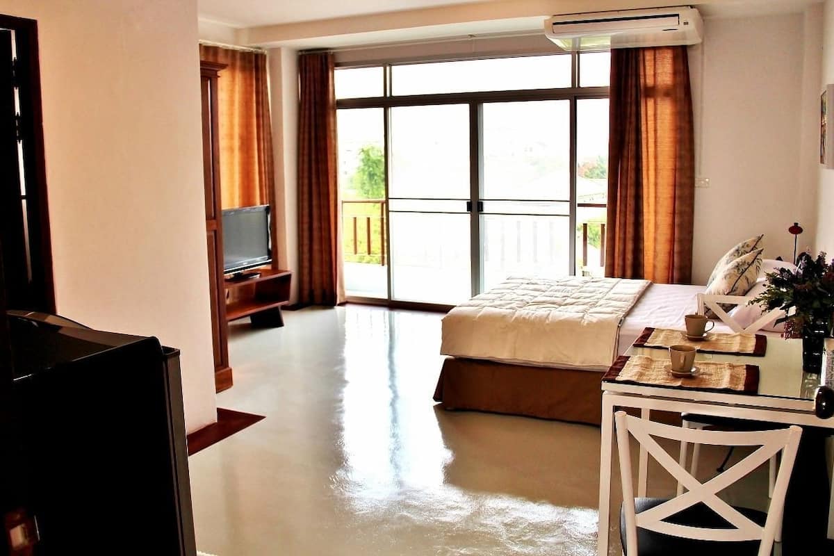 Ein Hotelzimmer mit einem Bett, einem Fernseher, einem Schreibtisch mit Stuhl und einem Balkon mit Vorhängen.