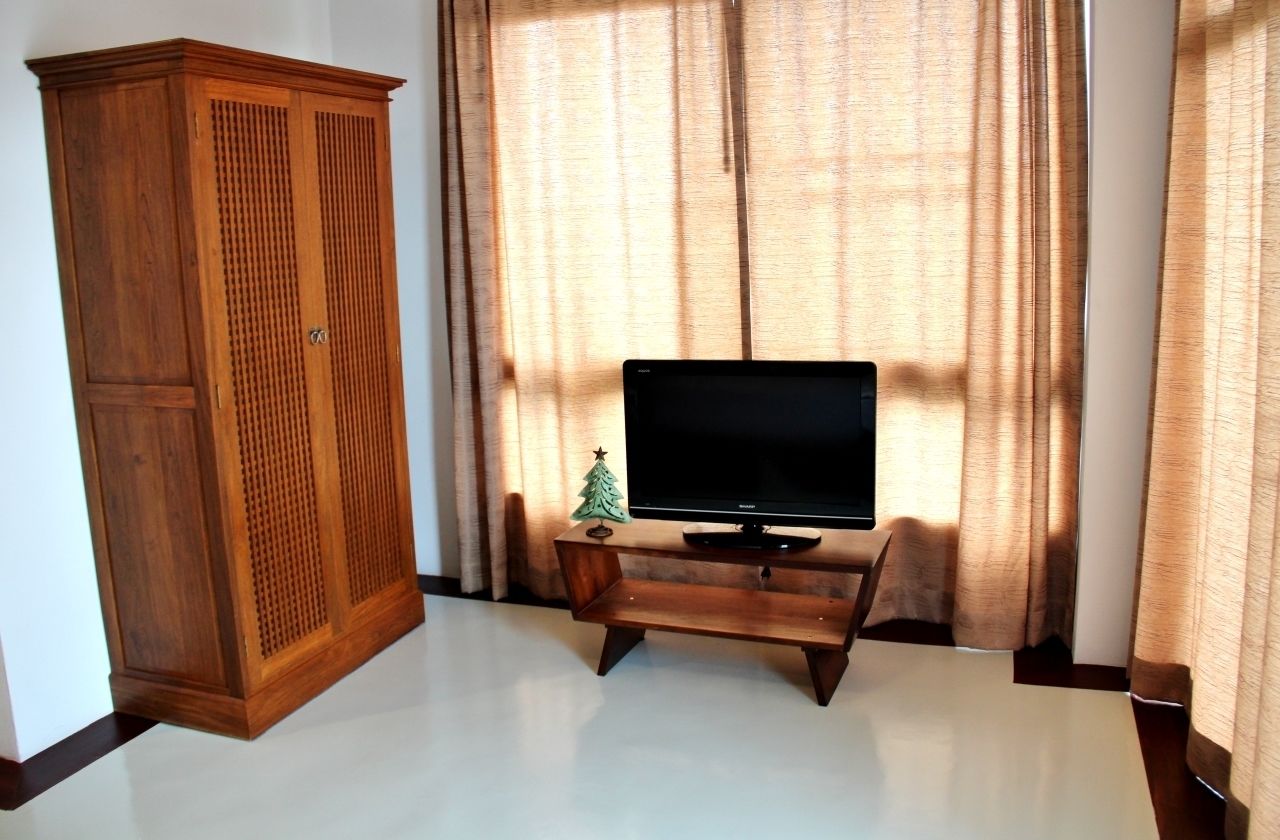 A room with a wooden wardrobe, a television on a wooden stand, and a small Christmas tree.