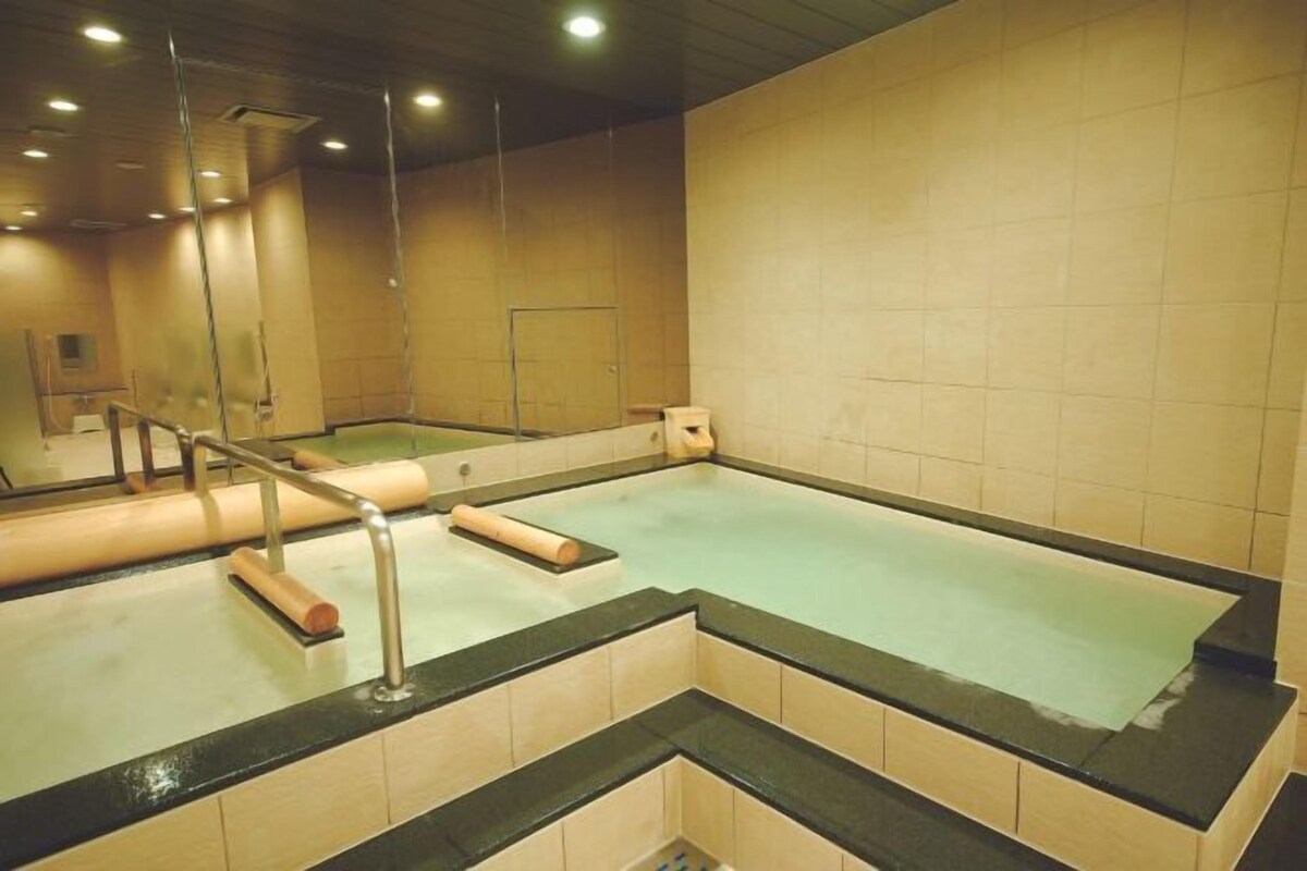 Una amplia piscina interior con pared de azulejos y barandilla de metal.