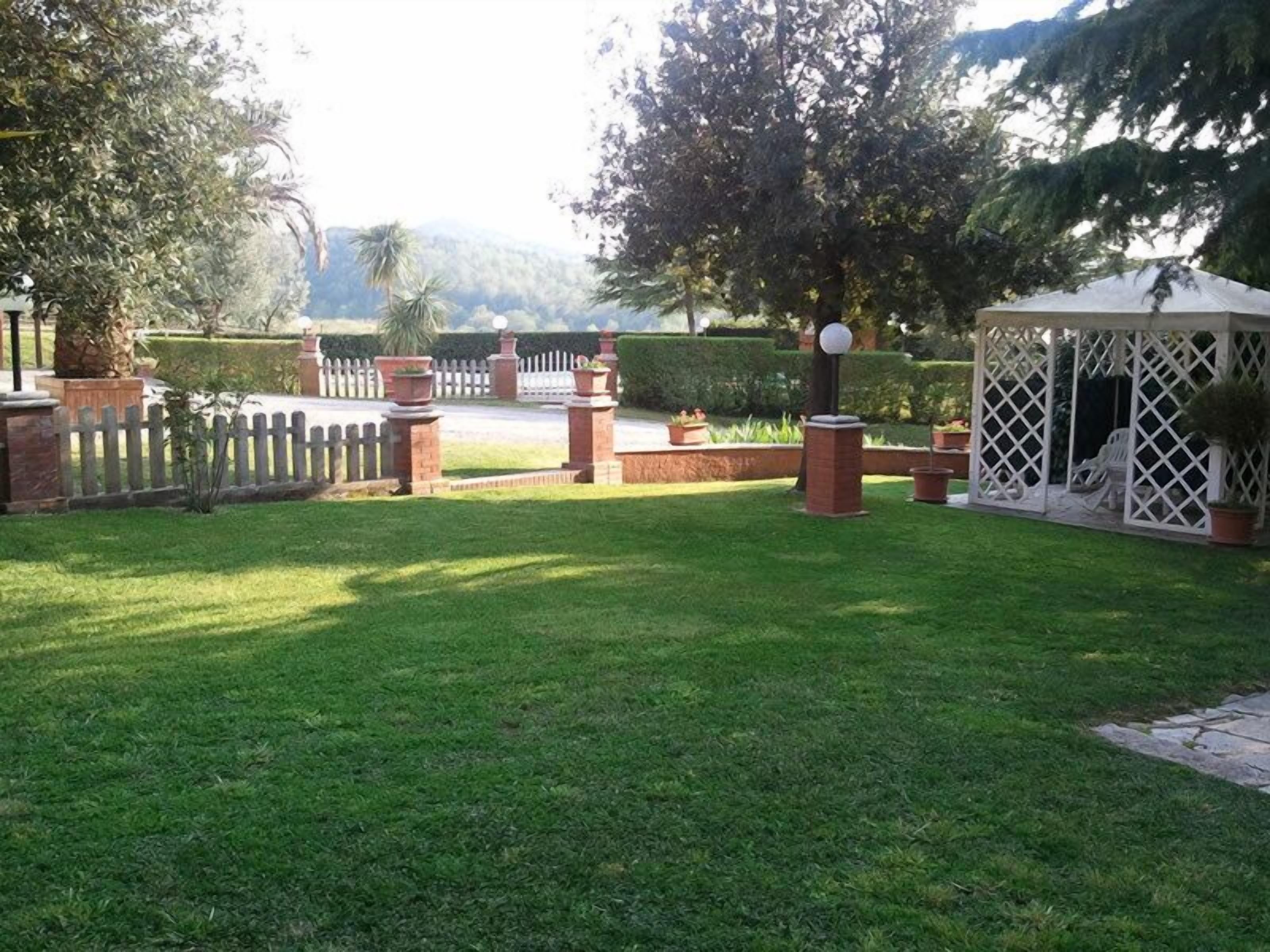 A well-maintained garden with a gazebo, a white fence, and a pathway leading to a body of water.