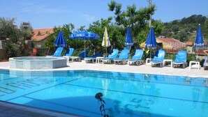 Una piscina con sillas y sombrillas azules, rodeada de vegetación y edificios.