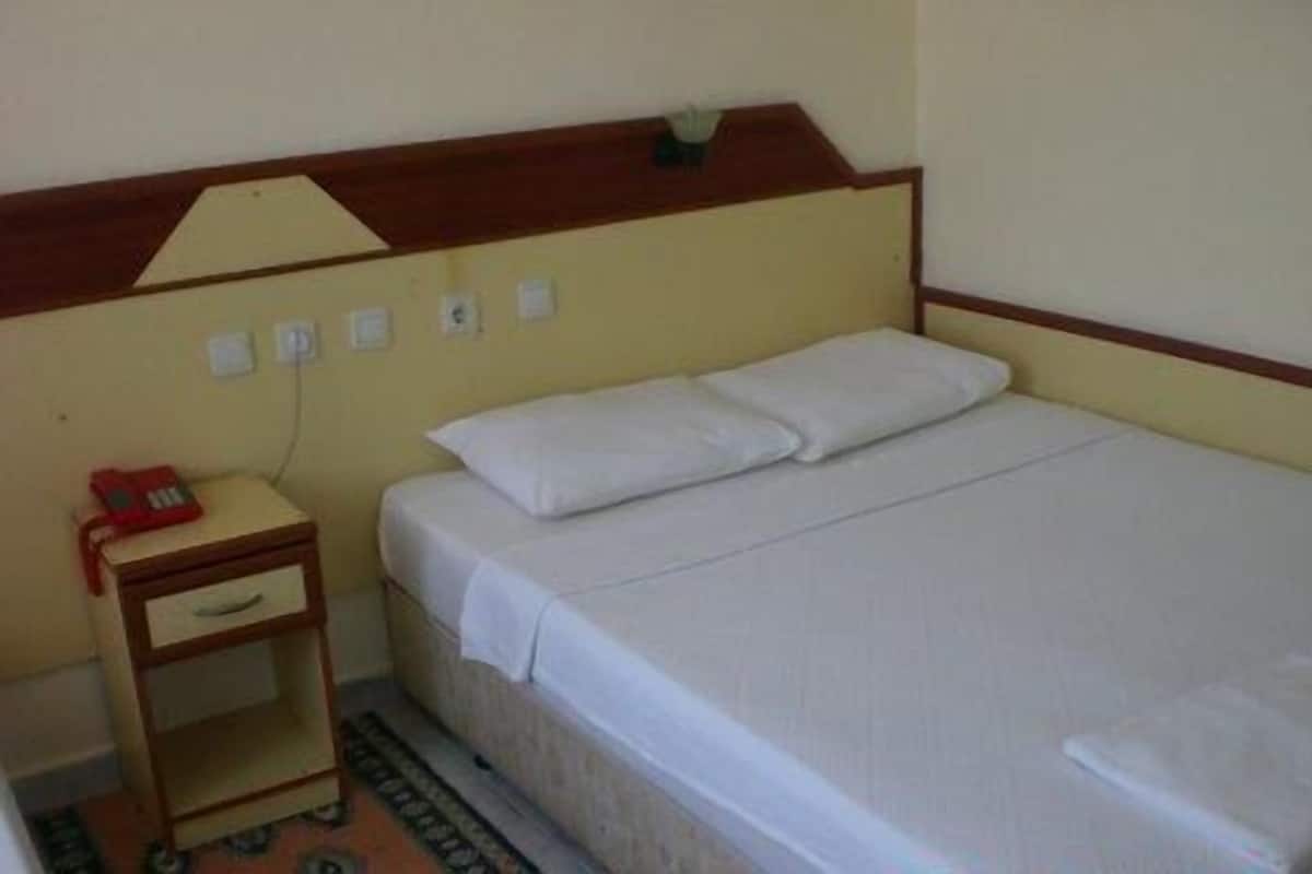 Una cama individual con ropa blanca en una habitación con cabecera de madera y una mesita de noche pequeña con un objeto rojo encima.