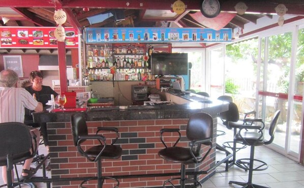 Un bar con mostrador de ladrillo, varios taburetes y una pantalla de televisión.