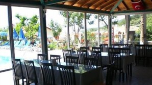 Un área de comedor al aire libre con mesas y sillas, con vistas a una piscina y follaje.