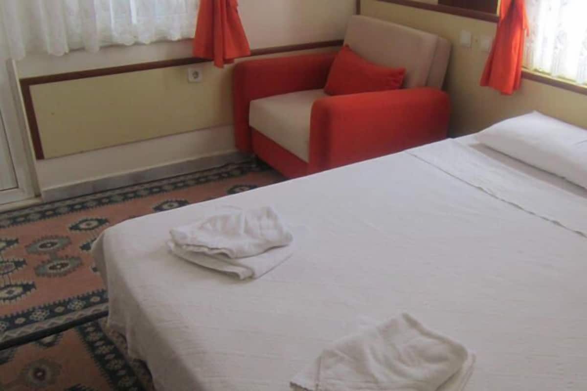 Una habitación de hotel con una cama, dos sillas rojas, una mesita y una ventana con cortinas.