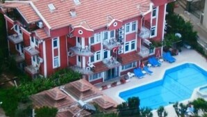 Un edificio rojo de varios pisos con balcones, piscina y mobiliario exterior.