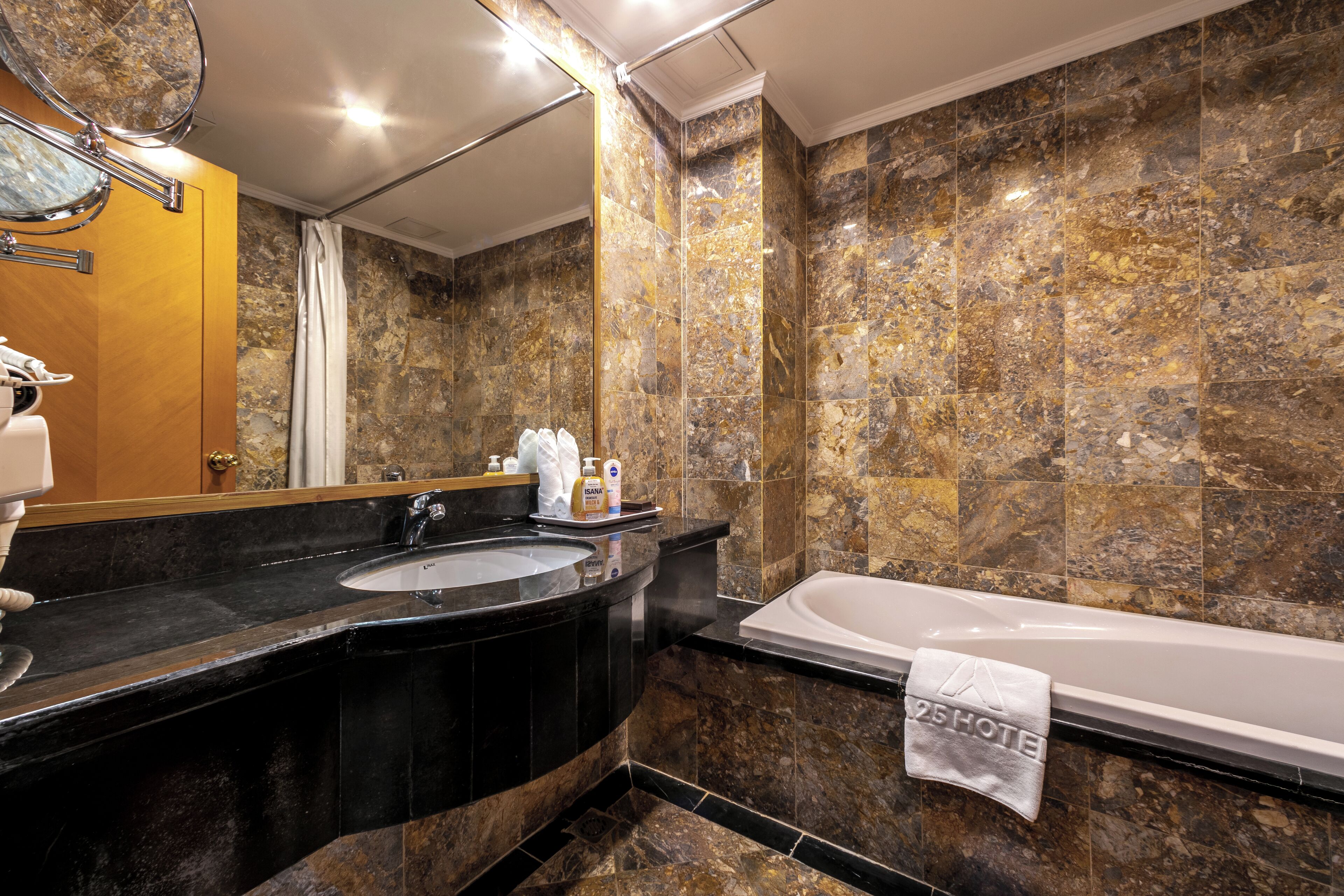 A bathroom with a marble wall, a sink, a mirror, and a bathtub.