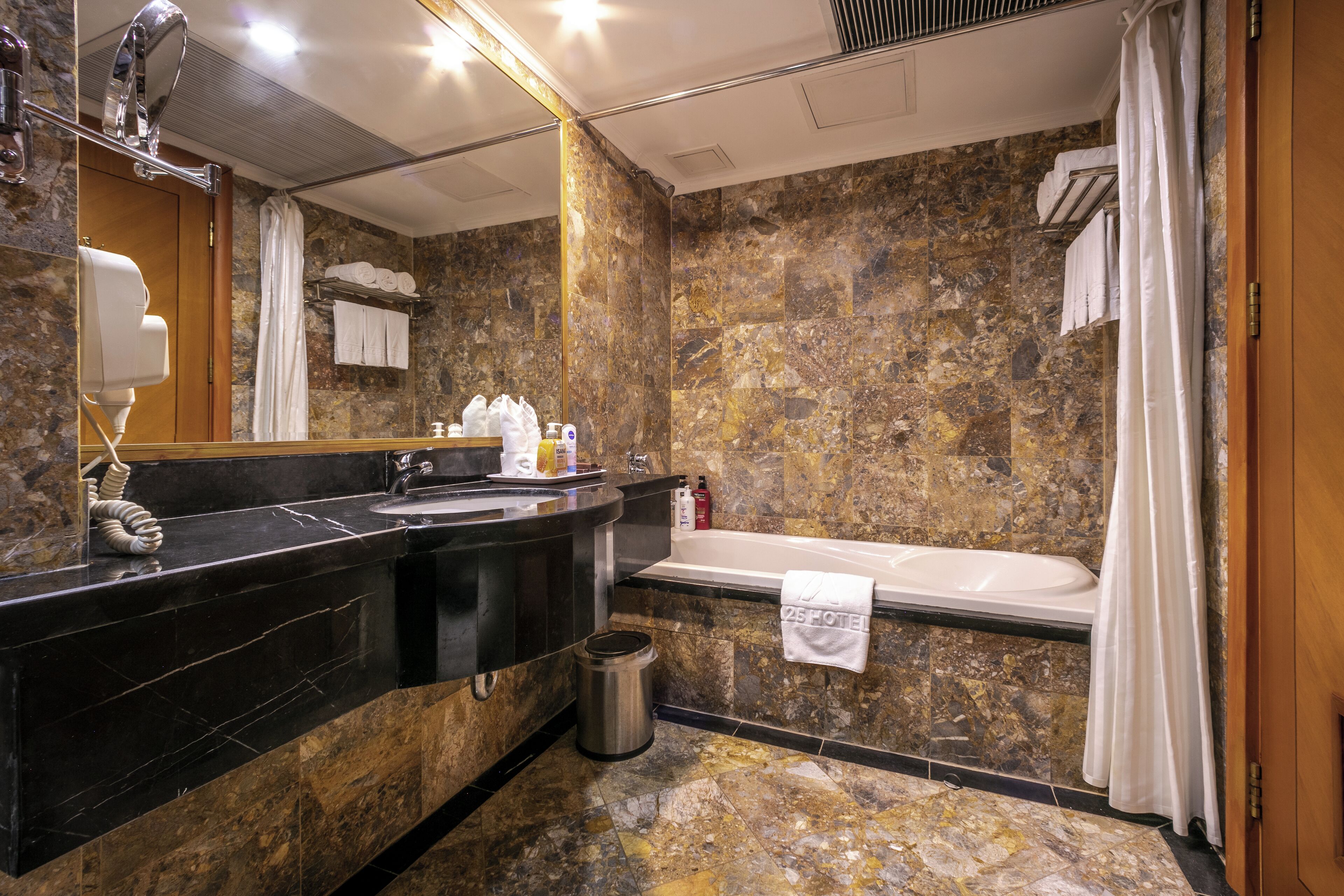 A bathroom with a marble wall, a bathtub, a sink, a mirror, and a towel rack.