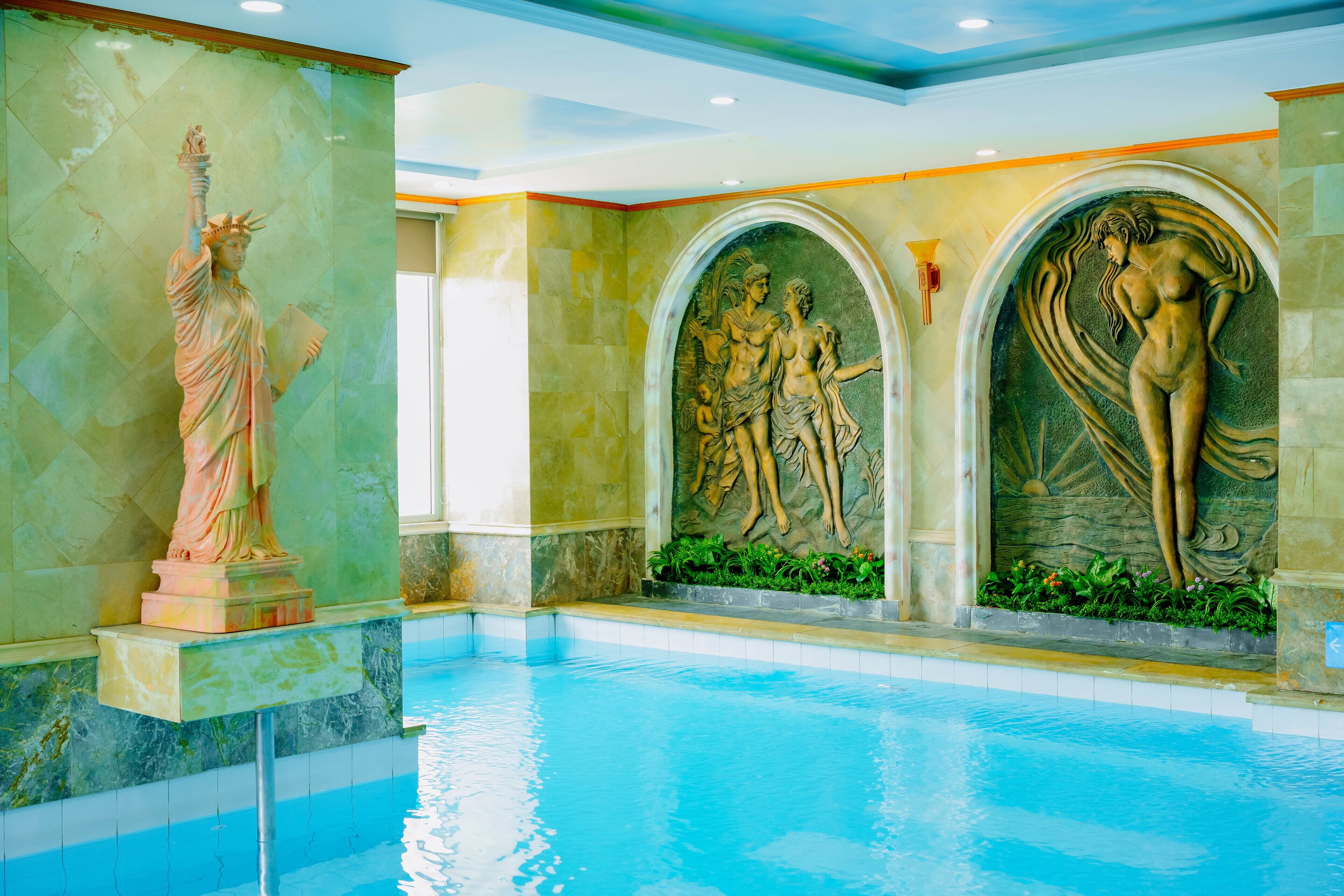 An indoor swimming pool with a statue of the Statue of Liberty and classical sculptures.