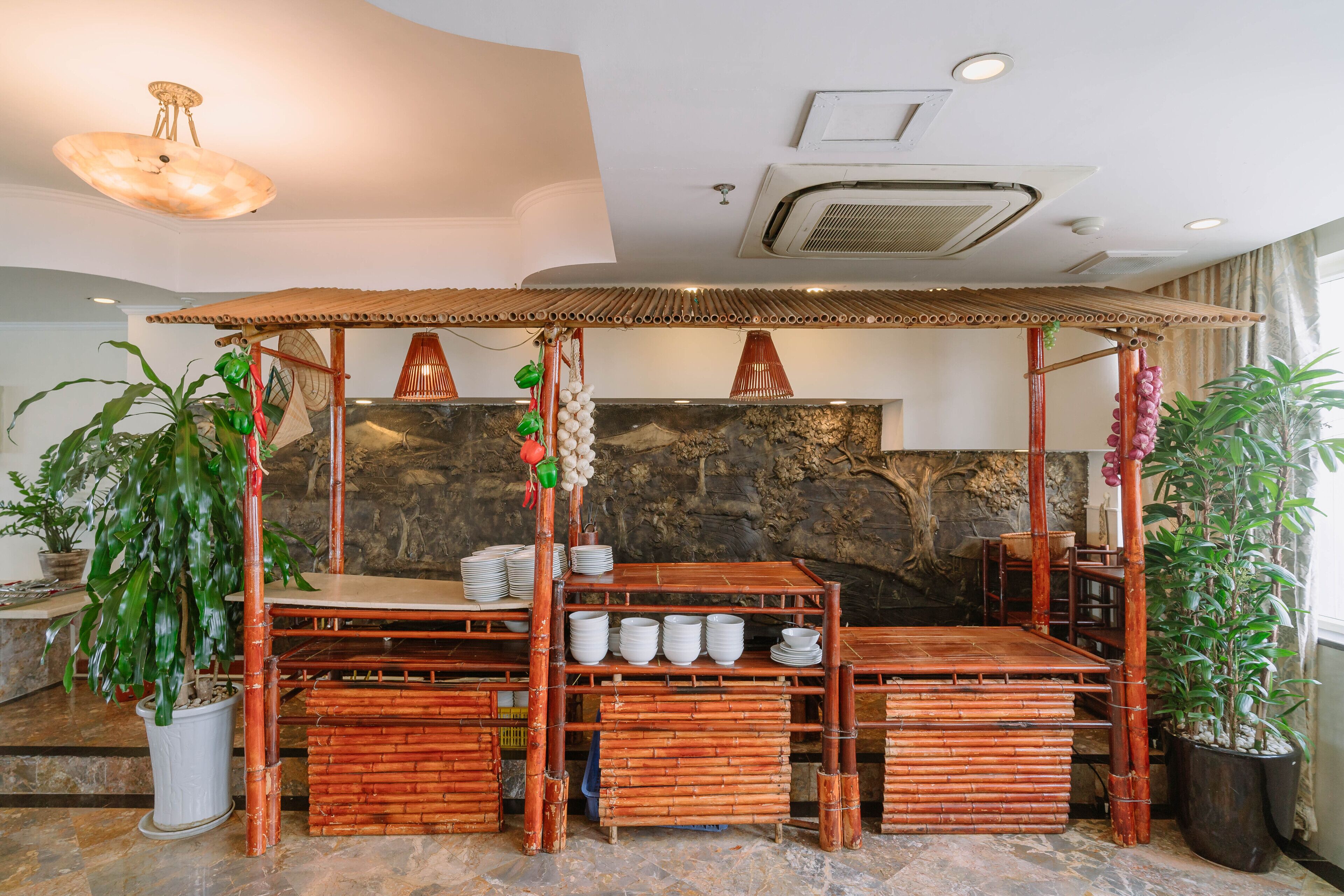 Una estructura de bambú con una mesa y sillas, rodeada de plantas en macetas.