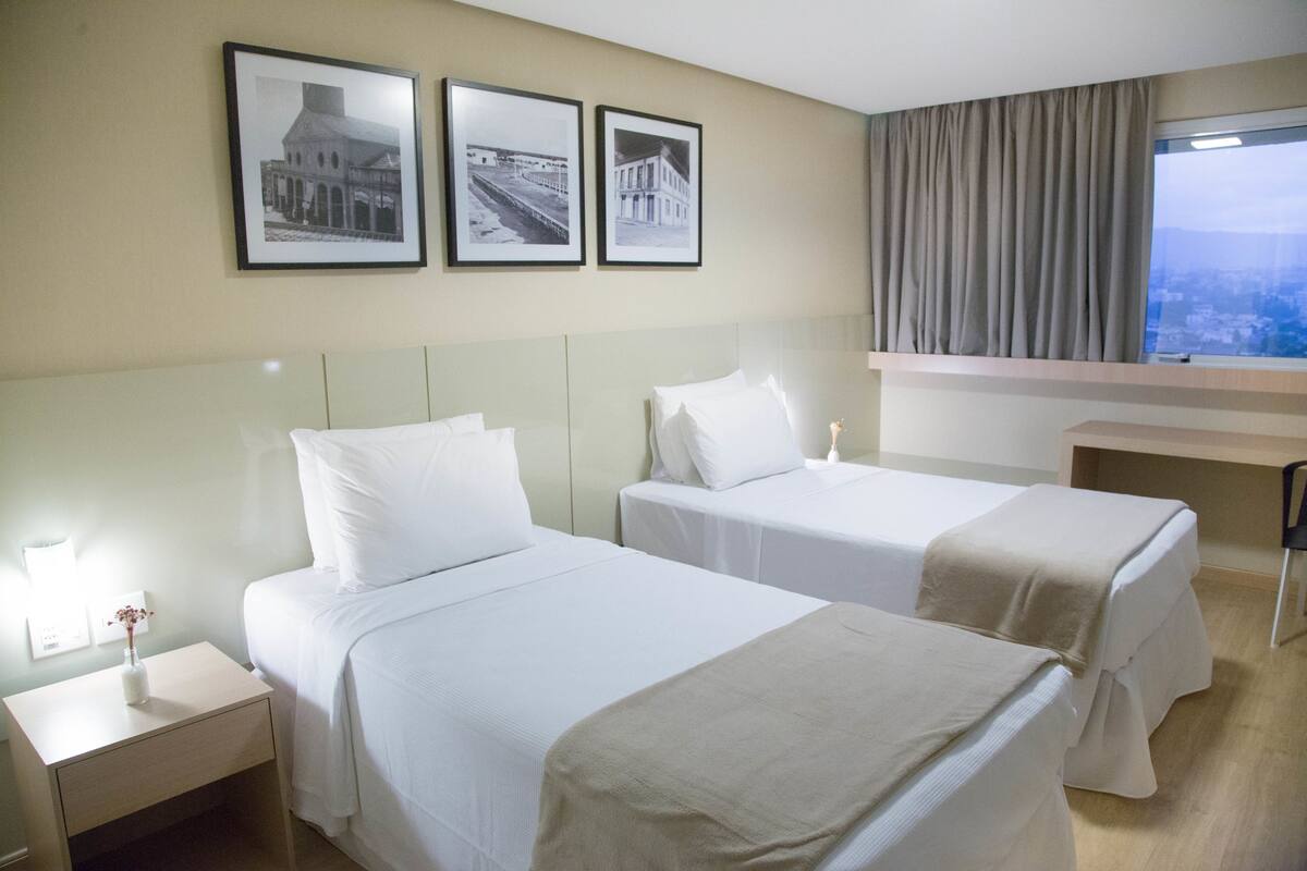 A hotel room with two beds, a nightstand, and a window with a view.