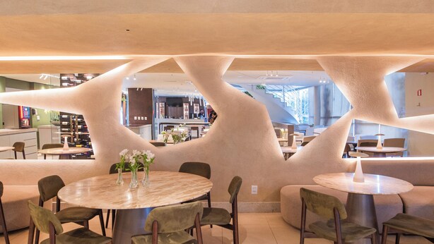 Un interior moderno con mesas y sillas redondas, una zona de bar y una escalera.