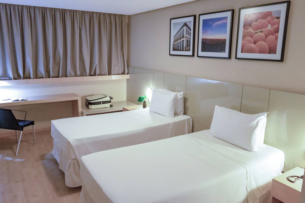 A hotel room with two beds, a desk, and a chair. There are framed pictures on the wall.