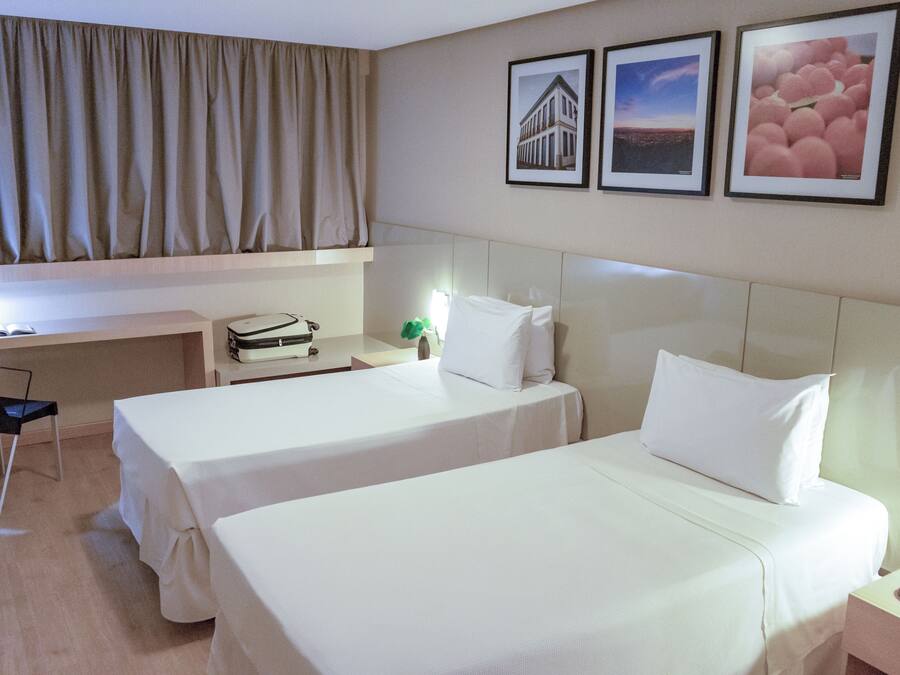 A hotel room with two beds, a desk, and a chair. There are framed pictures on the wall.