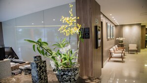 Zona de recepción con mostrador, una orquídea en maceta y un área de estar con sillones.