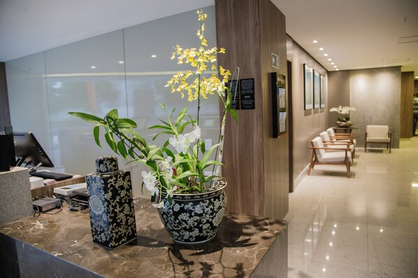 A reception area with a reception desk, a potted orchid, and a seating area with chairs.