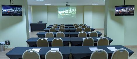 A conference room with tables and chairs, a projection screen, and two mounted TVs.