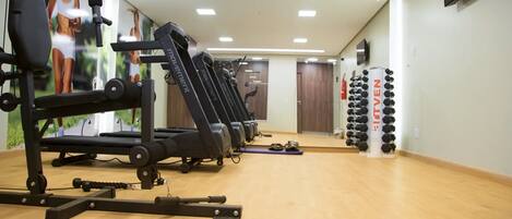 A gym with exercise equipment, a mirror, and a wall-mounted dumbbell rack.