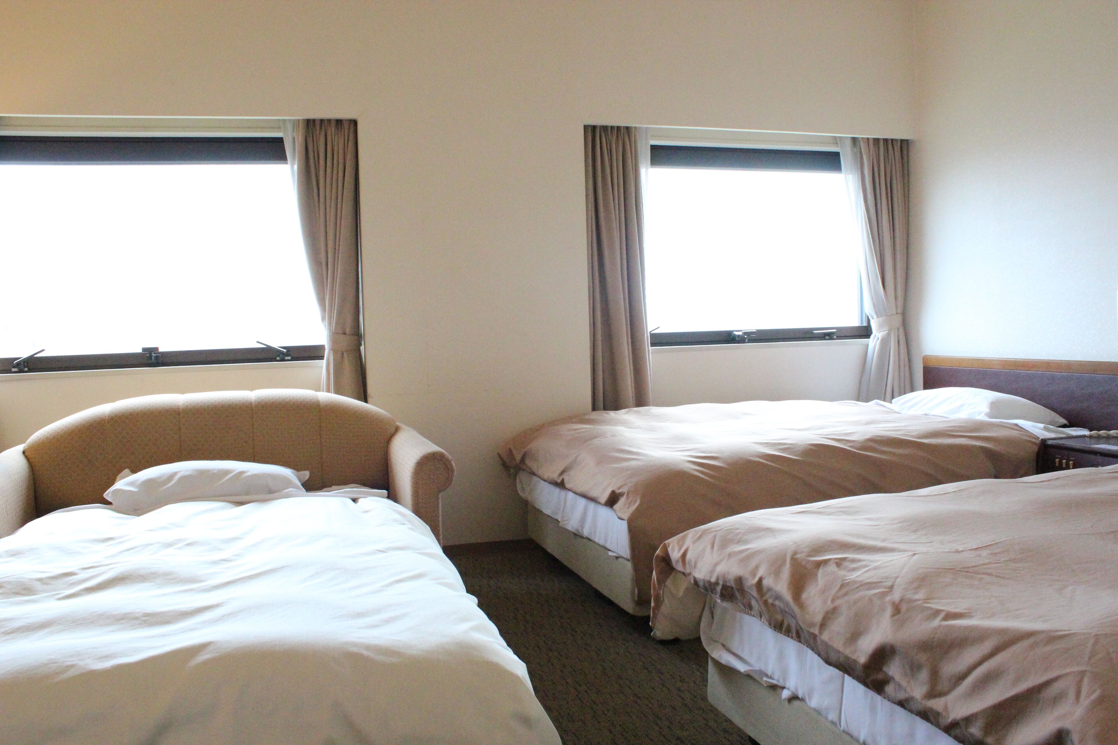 A hotel room with two single beds, a chair, and a window with curtains.