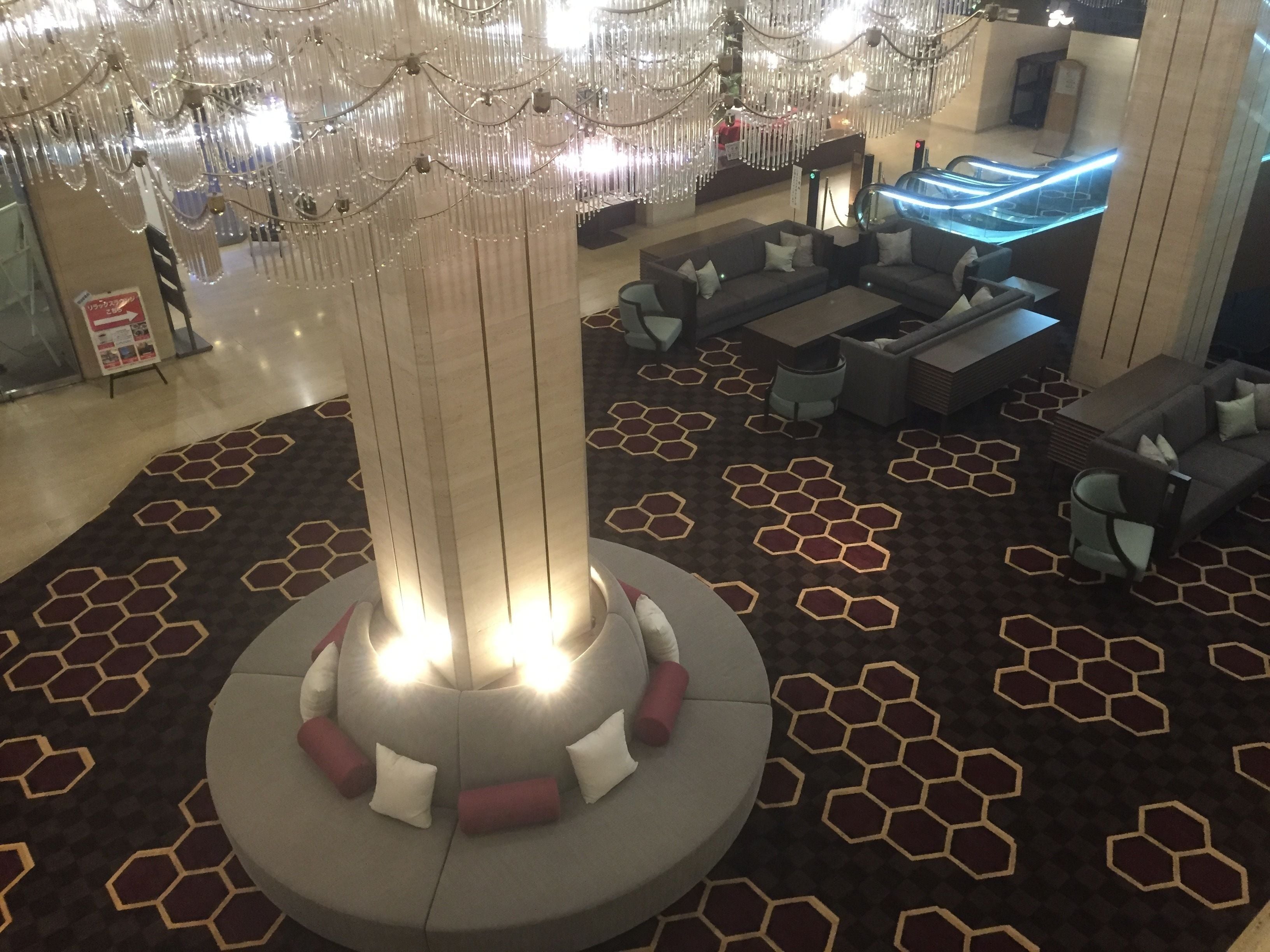 A lobby with a central seating area, hexagonal patterned carpet, and a modern chandelier.