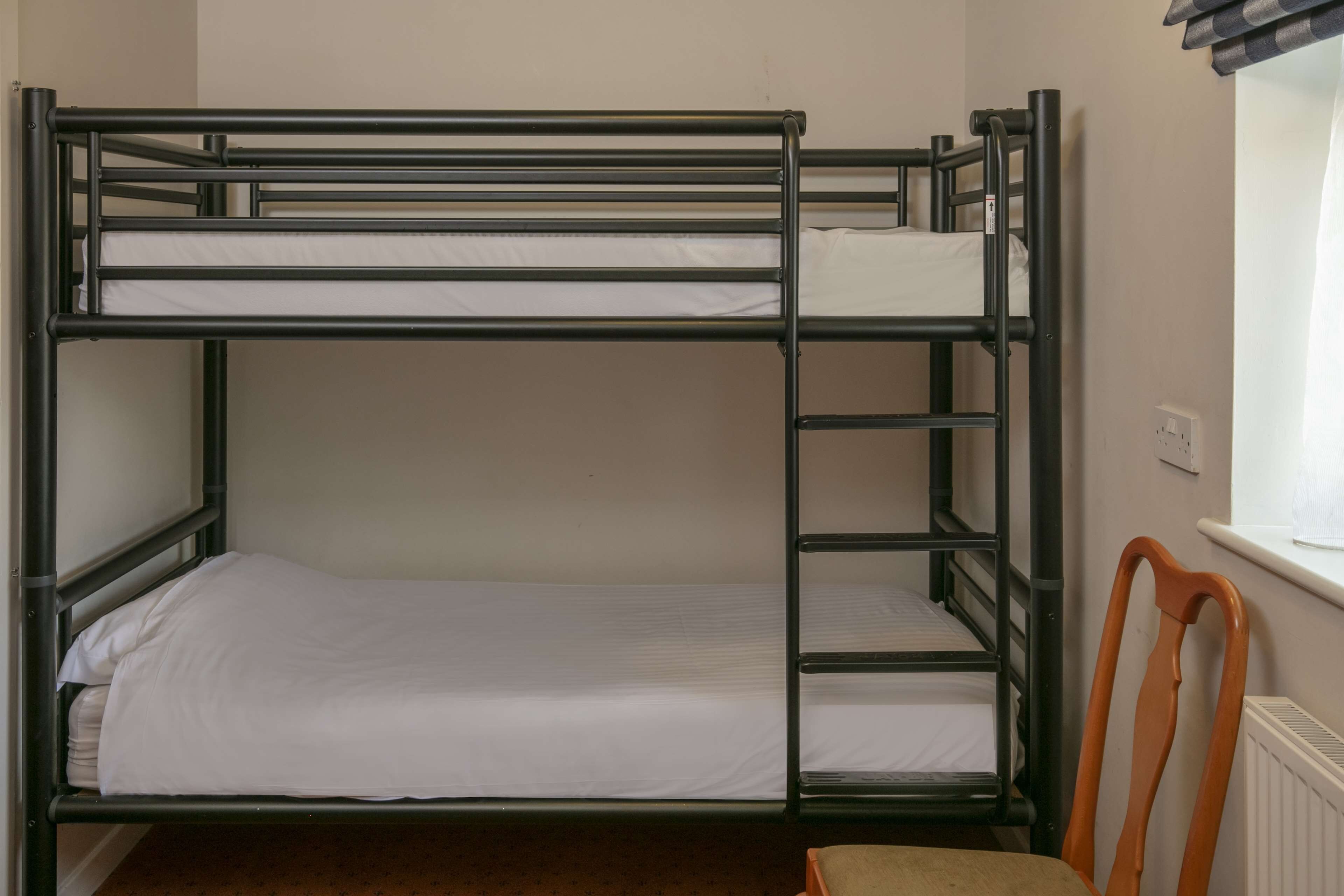 A bunk bed with a wooden chair and a window with blinds.