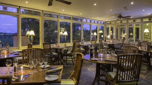 A restaurant with multiple tables and chairs, large windows with views of the outdoors, and ceiling fans.