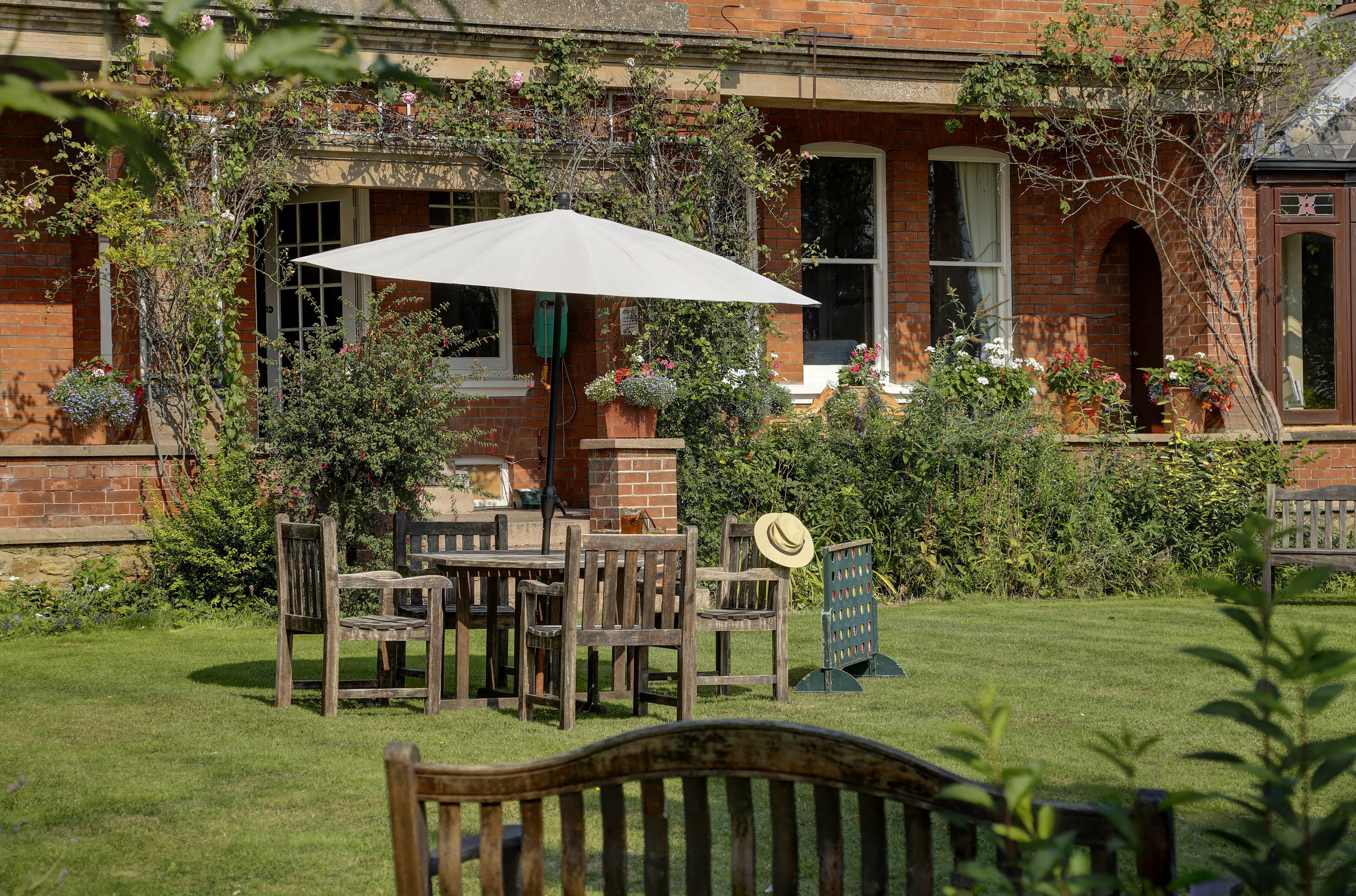Un bâtiment en briques doté d’un patio-jardin aménagé avec des meubles en bois et un parasol blanc.