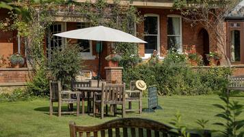 Un bâtiment en briques doté d’un patio-jardin aménagé avec des meubles en bois et un parasol blanc.