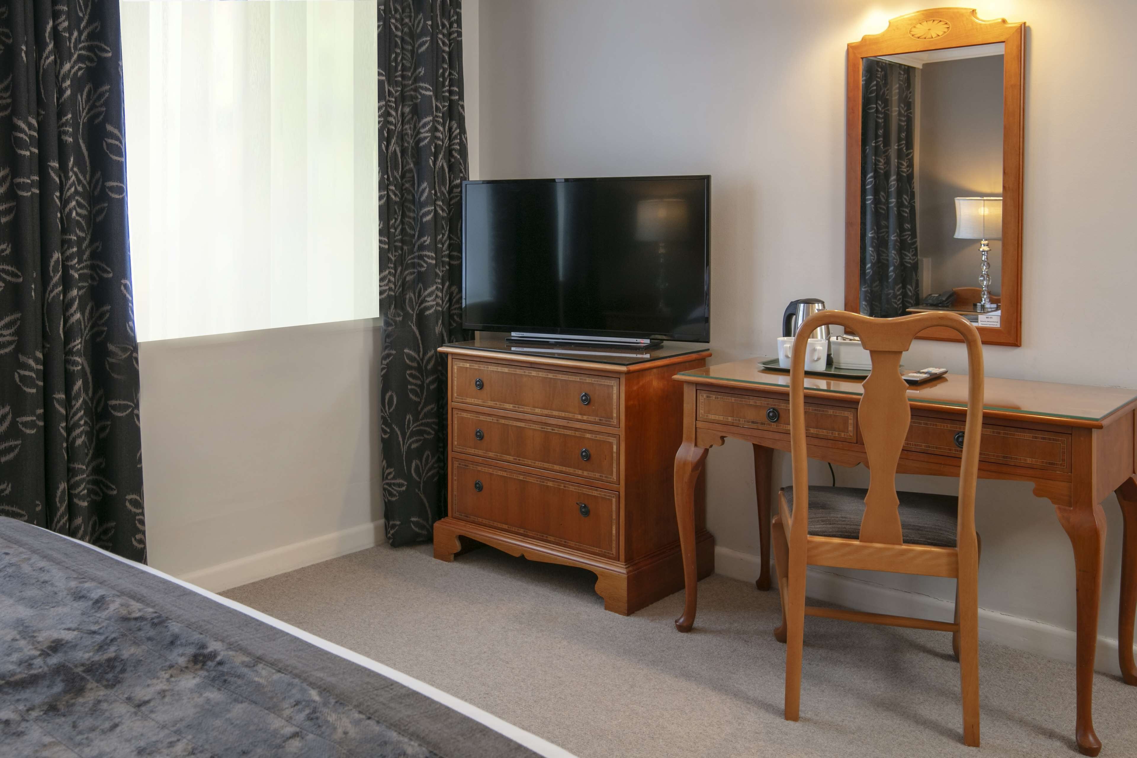 A hotel room with a wooden desk, a flat-screen TV, a dresser, and a mirror.