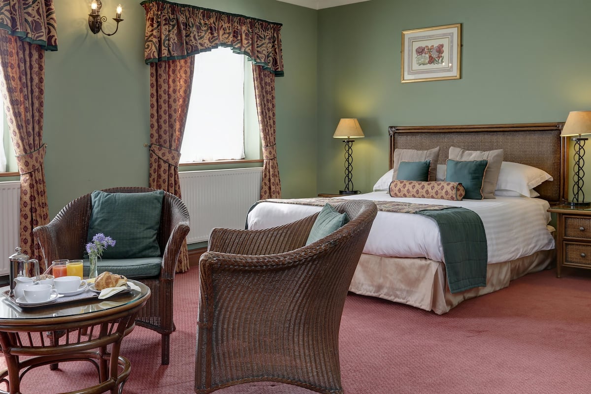 A bedroom with a large bed, two bedside tables, a chair, a table with breakfast items, and curtains.