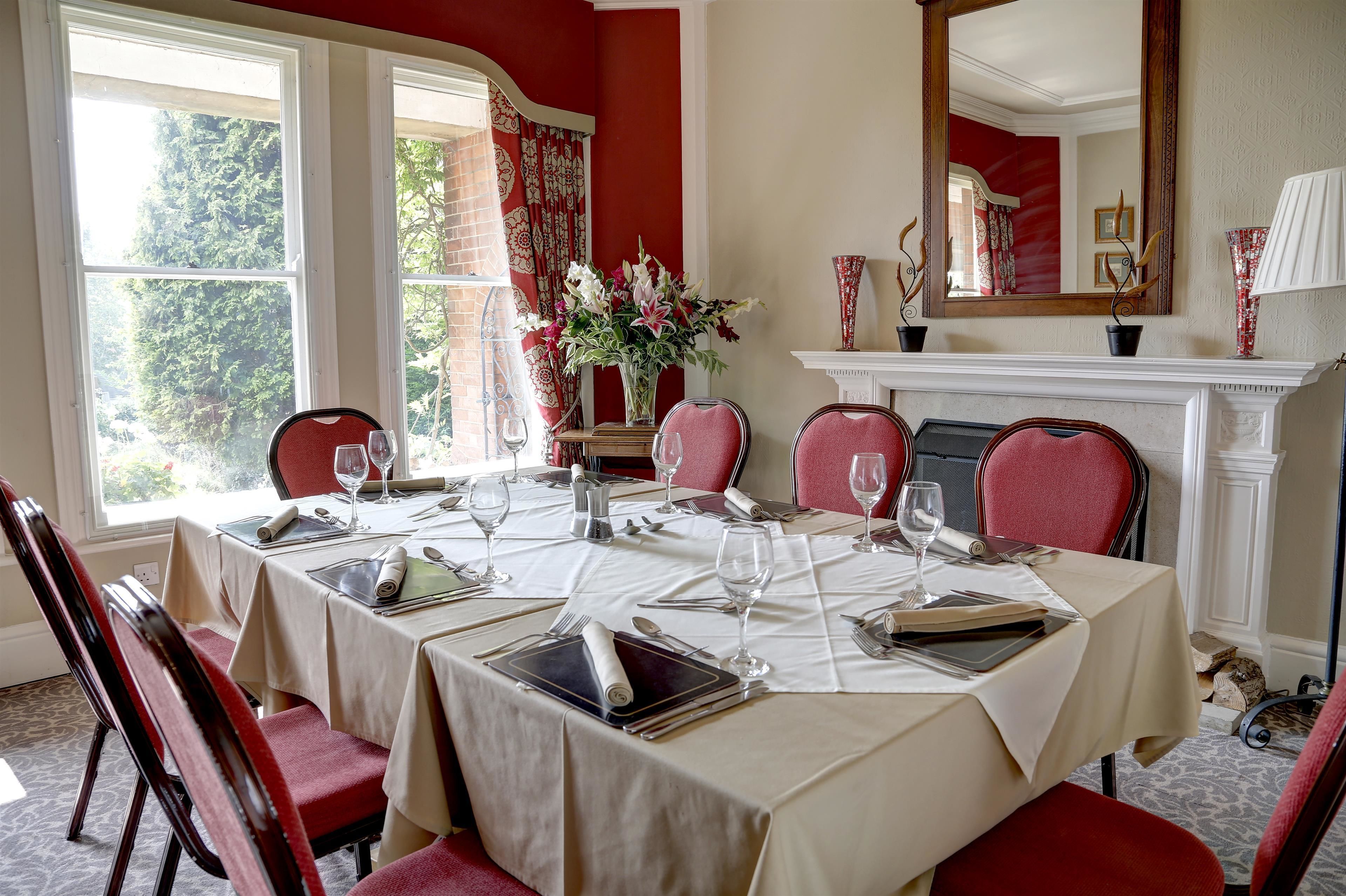 A dining room with a table set for six, red chairs, a vase of flowers, and a fireplace.